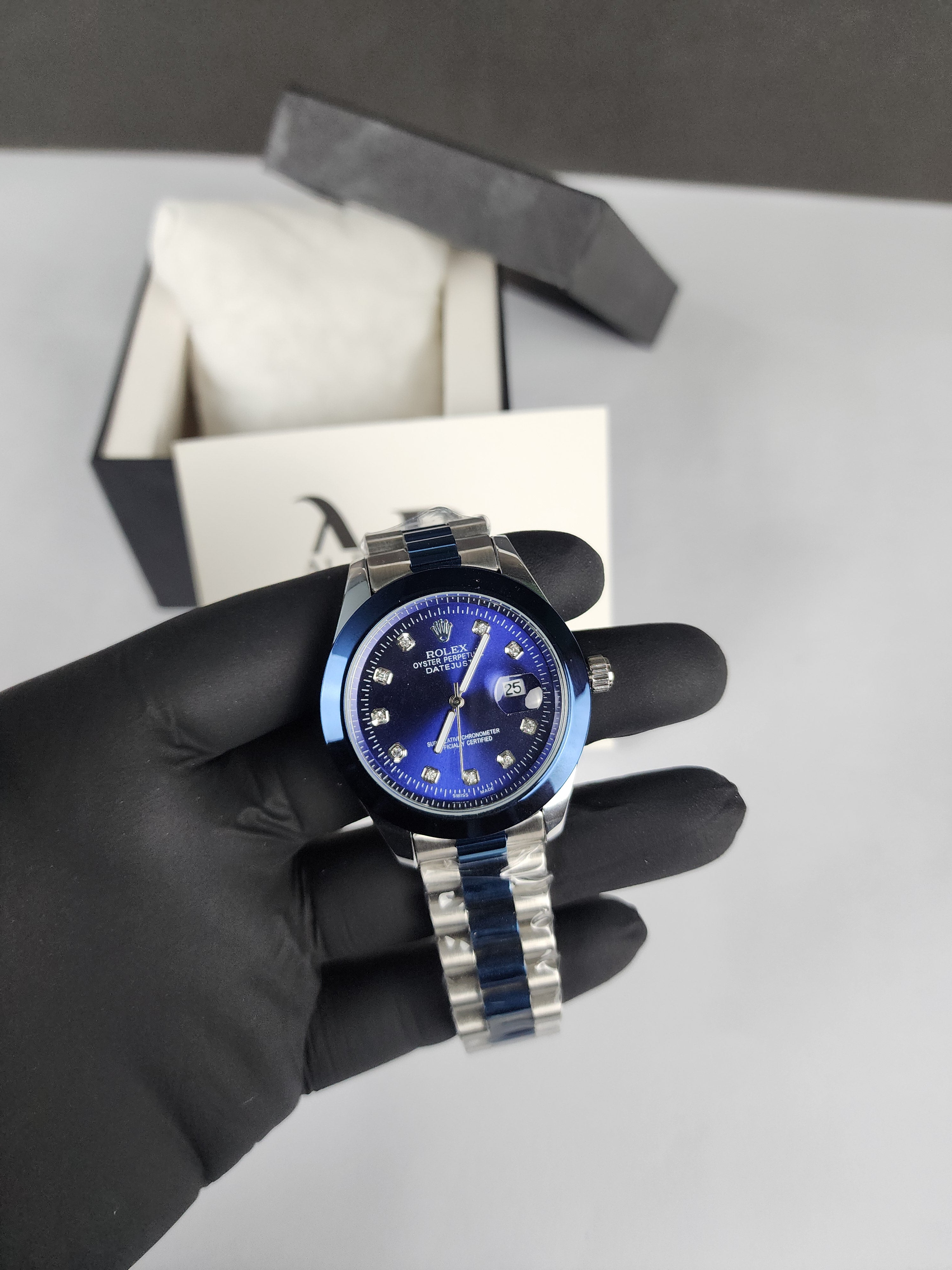 Hand wearing a black glove holding a silver and blue watch with a gray background