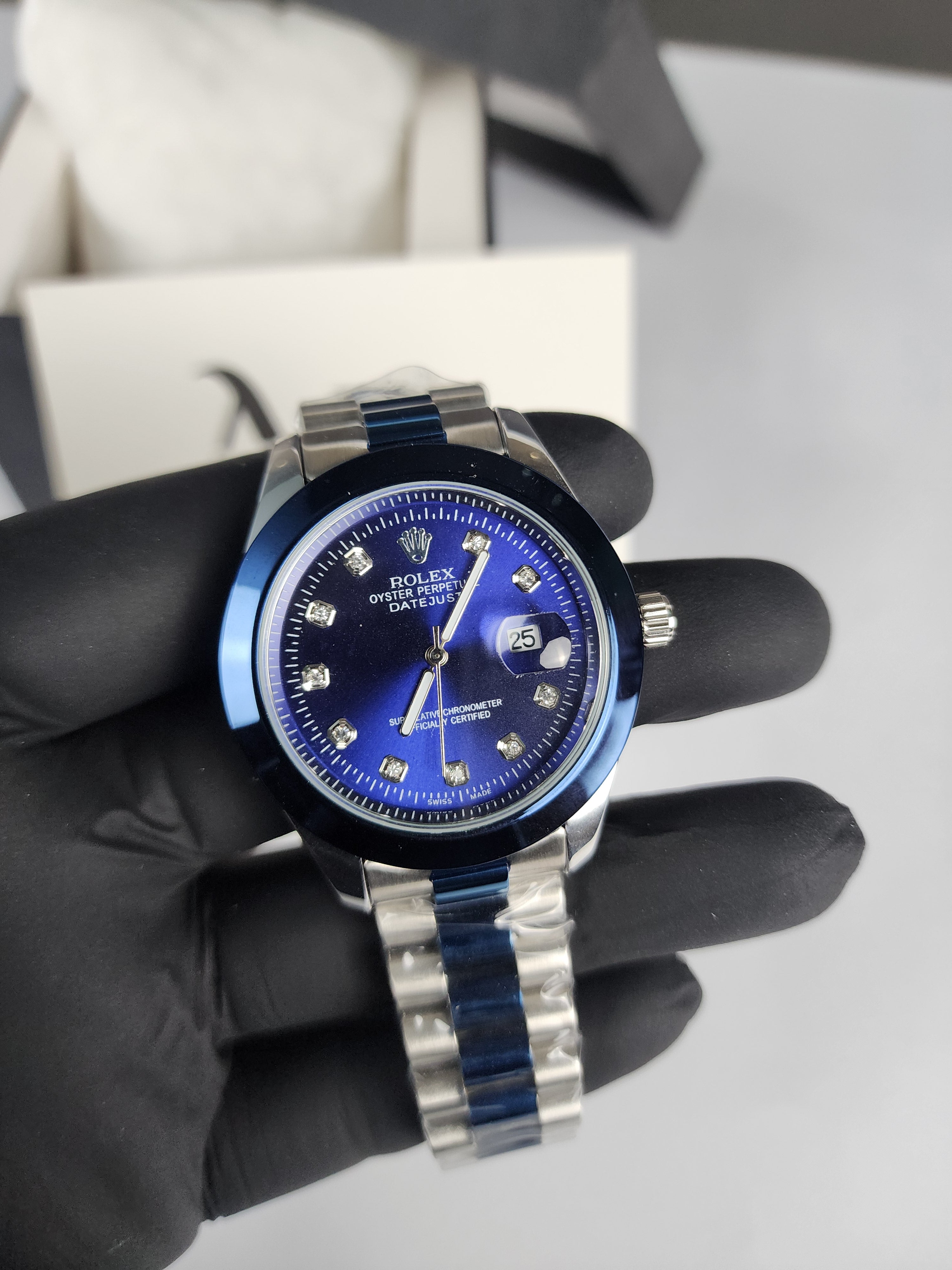 Watch with blue face and silver band held by a gloved hand against a neutral background