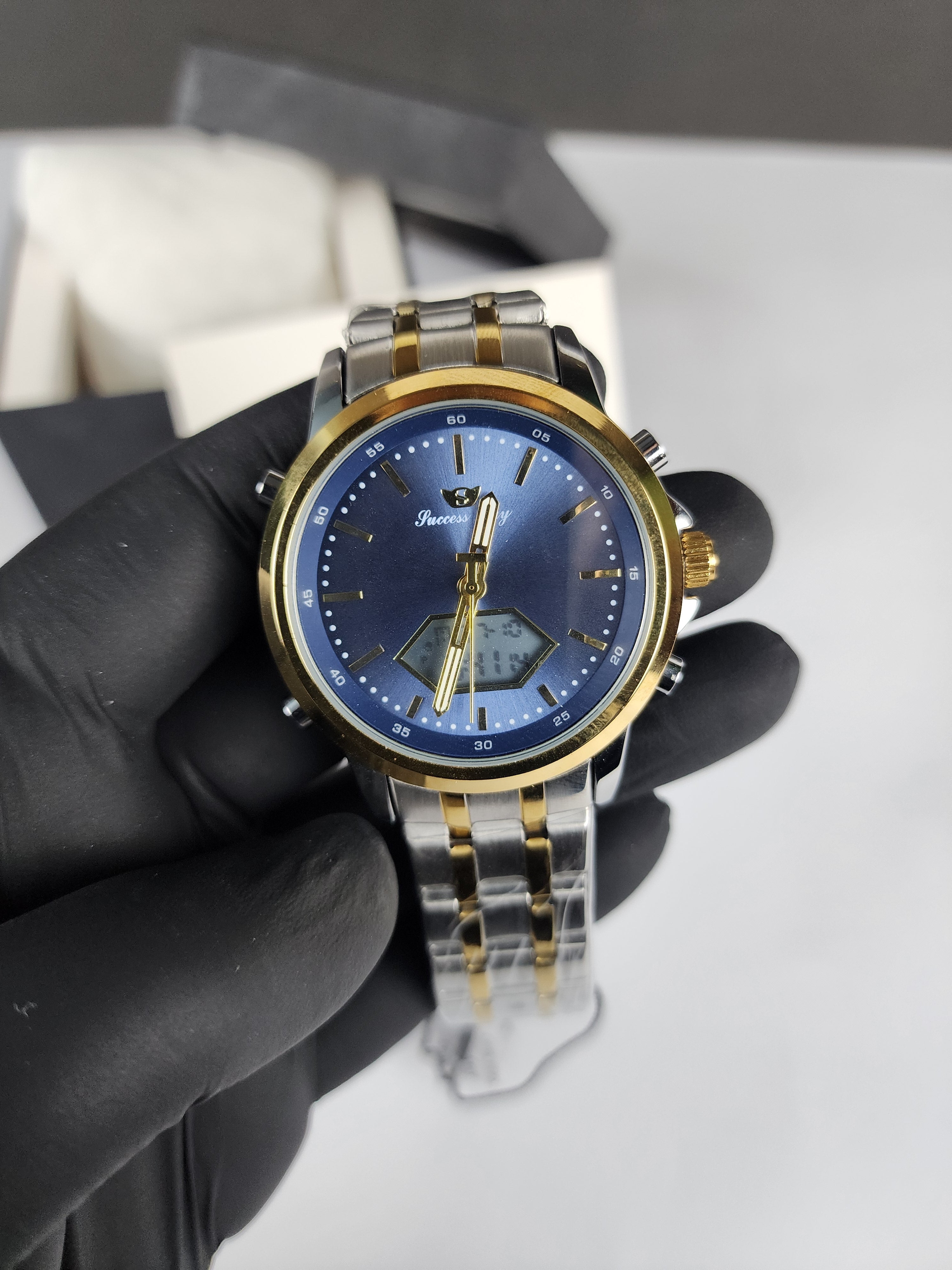 Gold and silver watch with blue face held by a gloved hand against a neutral background