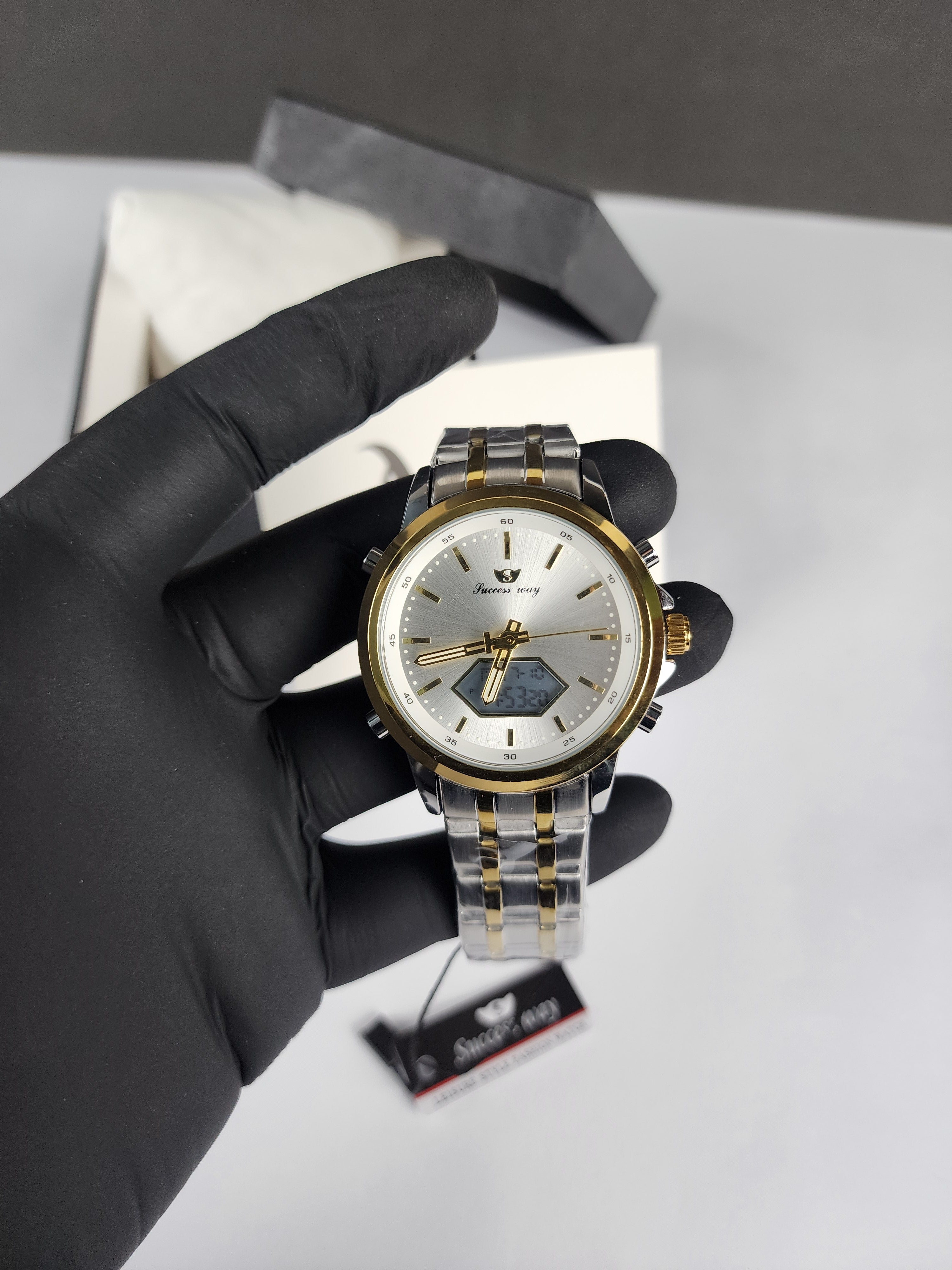 Hand wearing a black glove holding a silver and gold watch on a light gray background