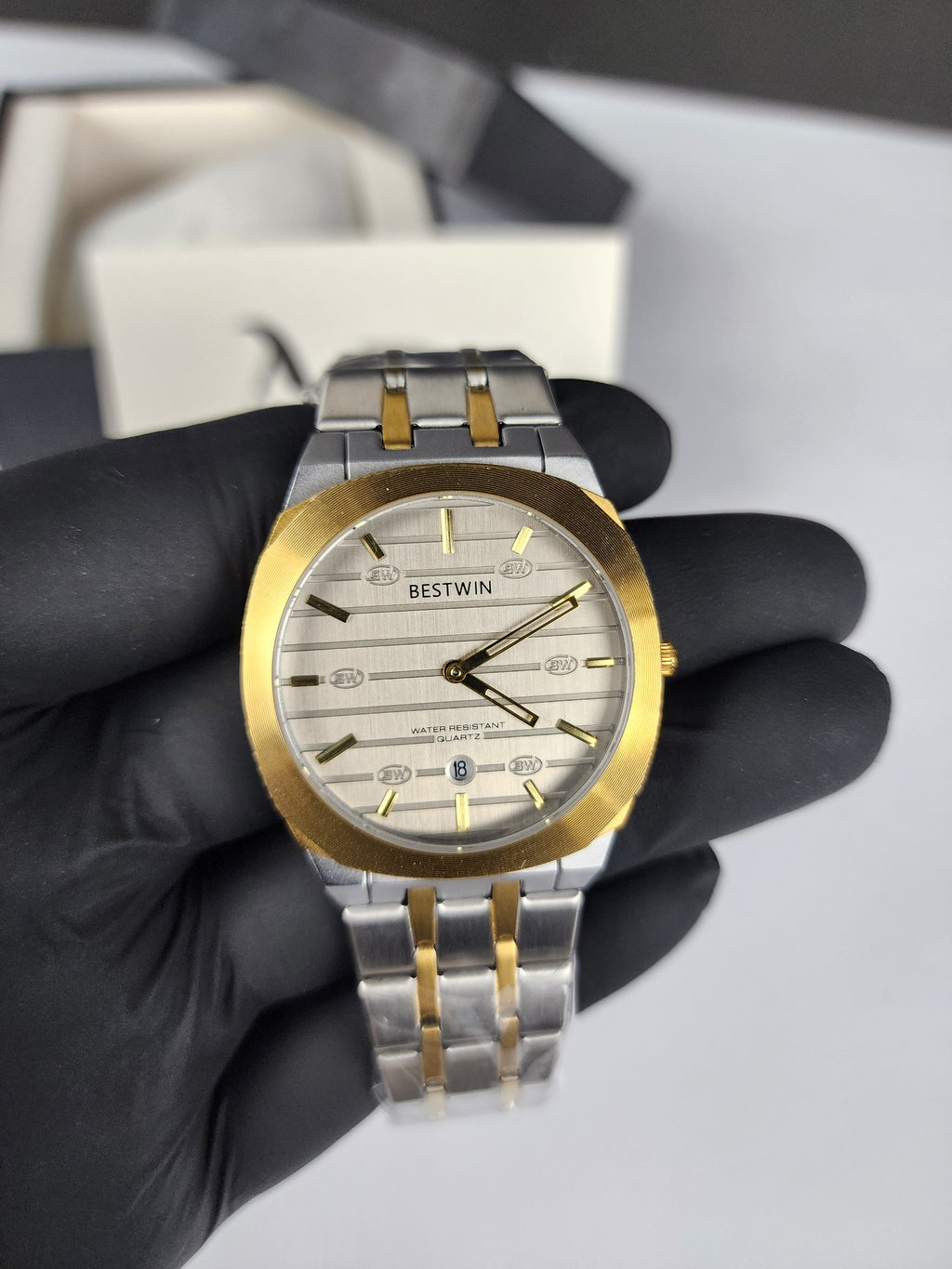 Watch with gold and silver band held by a gloved hand against a neutral background