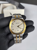 Watch with gold and silver band held by a gloved hand against a neutral background