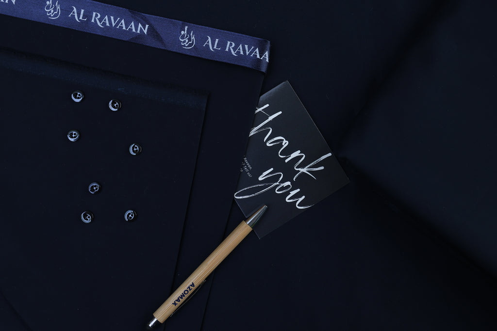 Dark shirt with buttons, a pen, and a 'thank you' card on a dark background with 'Al Ravaan' branding.