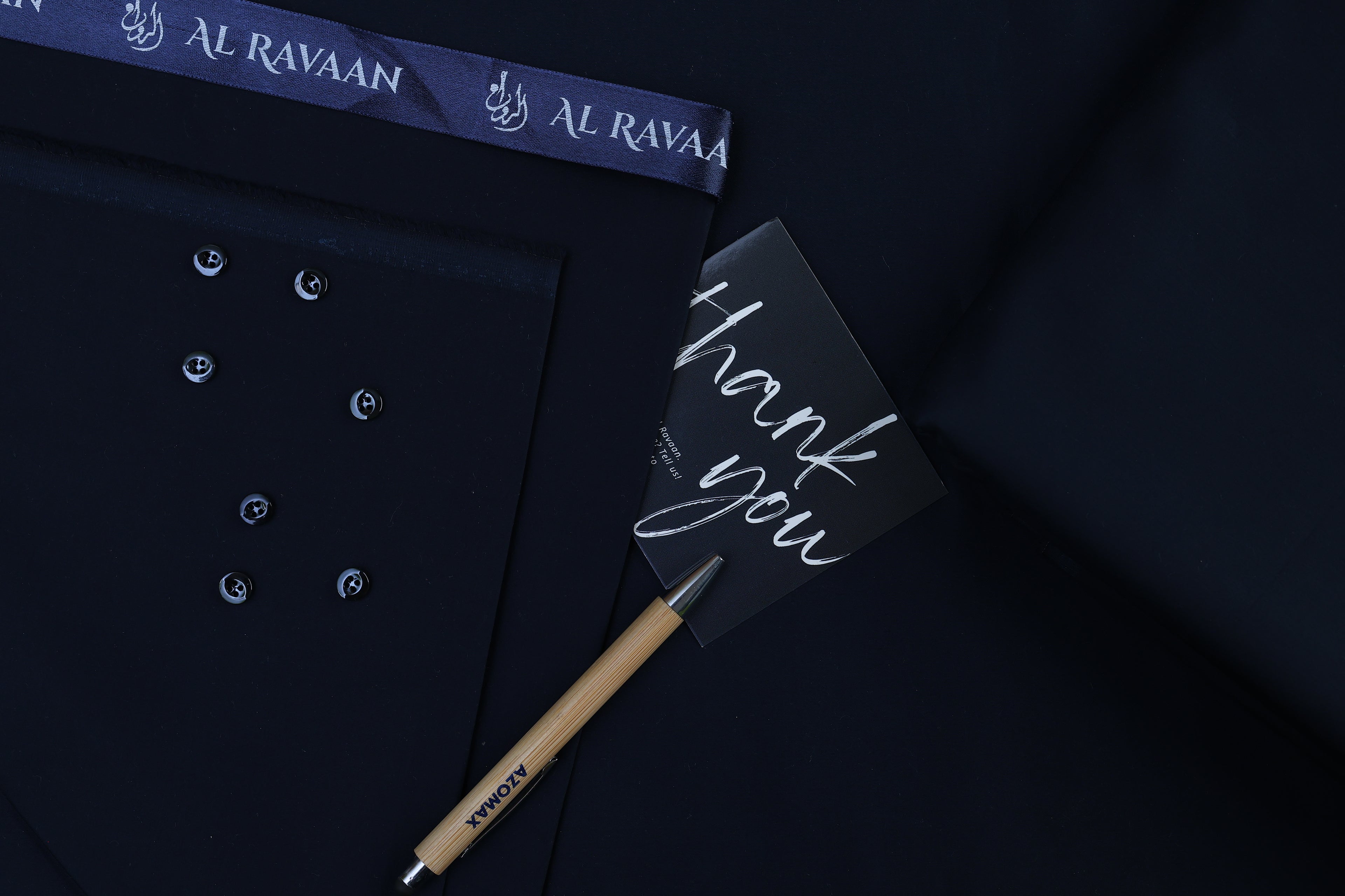 Dark shirt with buttons, a pen, and a 'thank you' card on a dark background with 'Al Ravaan' branding.