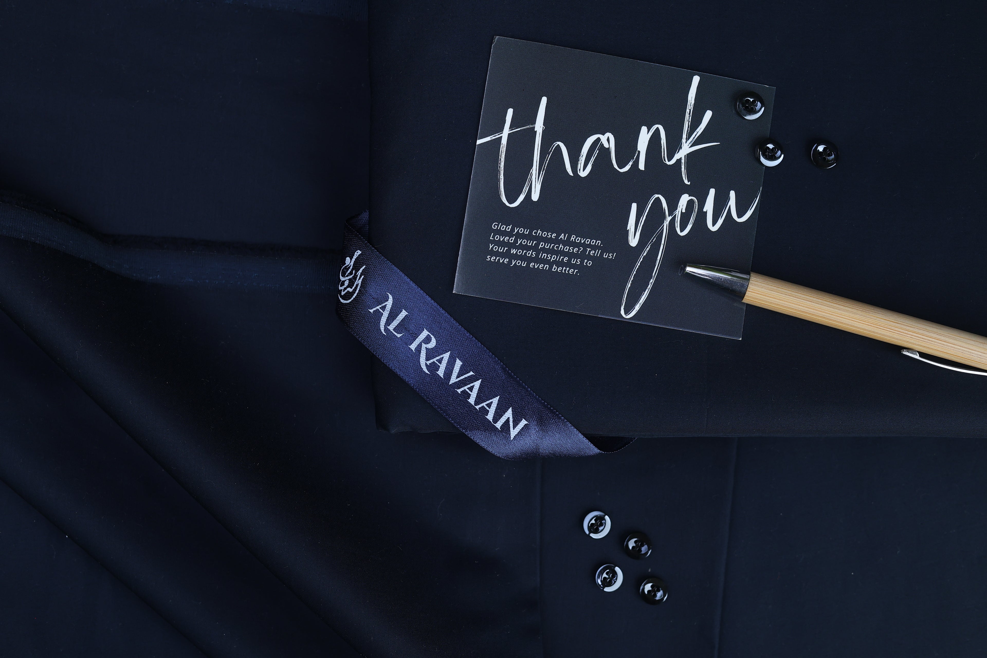 Navy blue shirt with a 'thank you' card and pen on a dark background